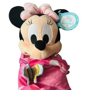May include: Pink and black plush Minnie Mouse doll wearing a pink blanket with a butterfly design. The doll has a pink bow and is holding a butterfly. The tag reads "Disney Babies".