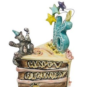 May include: A ceramic cake figurine with a cat on top and the words "Happy Birthday" on the side. The cake is decorated with stars and a blue number 16.