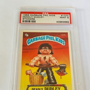 May include: A Garbage Pail Kids trading card featuring Deadly Dudley, a character with a black eye patch, a red bandana, and a bloody axe. The card is graded PSA 9, MINT 9, and has the number 137b on it.