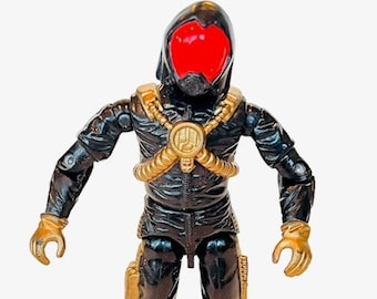 May include: A black action figure with a gold chest piece and a red visor. The figure is wearing a black hooded jumpsuit and has gold accents on the arms and legs.