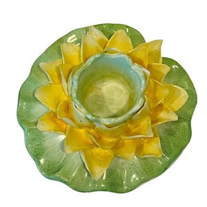 Może przedstawiać: Ceramiczny świecznik w kształcie żółtej lilii wodnej z zielonymi liśćmi. Świecznik ma centralne zagłębienie na świecę.