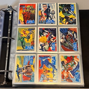 Könnte beinhalten: Eine Sammlung von Batman-Sammelkarten im Vintage-Stil in einem Ordner. Die Karten zeigen farbenfrohe Comic-Illustrationen von Batman, Robin und verschiedenen Schurken. Jede Karte trägt einen Titel wie "Cornered on a Cliff" und "Routing the Riddler".
