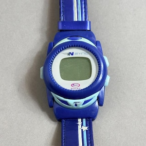 May include: Blue digital watch with a matching blue strap. The watch face has the text "N SYNC" and "ROCKS". The strap features white and light blue stripes and star accents. The watch is a vibrant blue color.