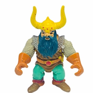 May include: A plastic action figure of a dwarf warrior with a yellow horned helmet, a blue beard, and a brown leather belt with a red jewel. The figure is wearing a grey chainmail shirt, brown leather pants, and orange gloves.