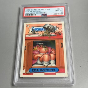 May include: A Garbage Pail Kids trading card titled "EDA MOUTHFUL" from 1988, graded GEM MT 10. The card features a cartoon illustration of a character with food in their mouth and a kitchen scene. The card is encased in a protective holder.