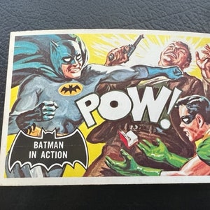 Könnte beinhalten: Eine Vintage-Comic-Karte mit Batman in Aktion. Die Karte zeigt Batman in einem blau-schwarzen Kostüm, das einen Mann in einem braunen Anzug schlägt. Der Text "POW!" ist in großen, fetten Buchstaben geschrieben. Die Karte zeigt auch den Text "Batman in Action".