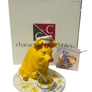 May include: A yellow pig figurine wearing a chef's hat and holding a spoon over a bowl of soup. The base of the figurine is white with the words "Ham Stir" written on it. The figurine is part of a collection called "Charactables".