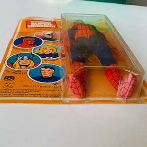 May include: A vintage action figure of Spider-Man in a red and blue suit with a black web design. The figure is packaged in a plastic blister pack with a yellow cardboard backing. The backing features images of other Marvel Super Heroes, including Thor, Invisible Woman, and Spider-Man. The text on the backing reads "Marvel Super Heroes!" and "Collectionne les Super Heros!"