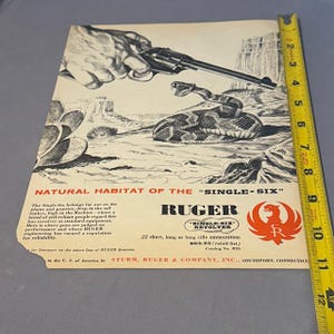 May include: Vintage advertisement for the Ruger Single-Six revolver. The image features a hand holding the revolver, a coiled rattlesnake, and a desert landscape. Text includes "Natural Habitat of the Single-Six" and "Ruger".