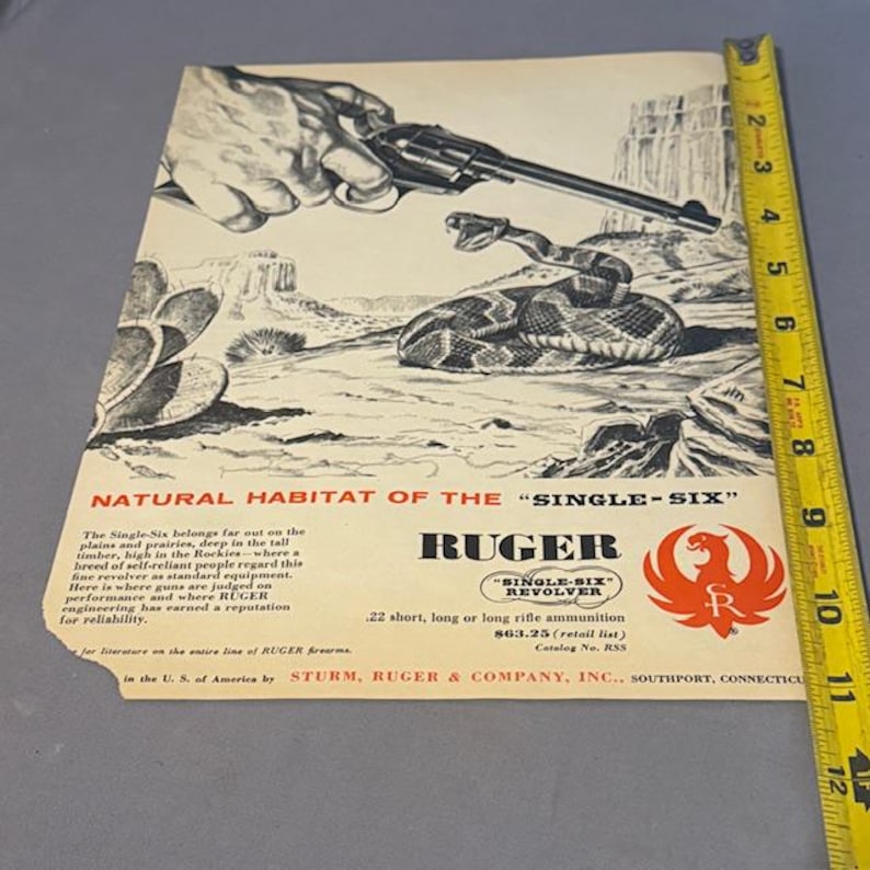 May include: Vintage advertisement for the Ruger Single-Six revolver. The image features a hand holding the revolver, a coiled rattlesnake, and a desert landscape. Text includes "Natural Habitat of the Single-Six" and "Ruger".