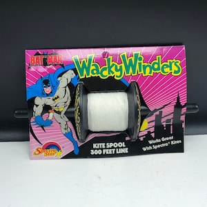 Può includere: Bobina per aquiloni Batman Wacky Winders con 91,44 metri di filo. La confezione presenta un'illustrazione di Batman e una silhouette di paesaggio urbano. La bobina è nera con filo bianco e loghi di Batman.
