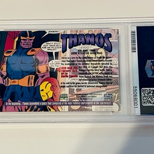 May include: A comic book card featuring Thanos, a purple supervillain from Marvel Comics. The card has a blue and yellow background with the text "THANOS" in large, white letters. The card also includes a small image of Iron Man in the lower right corner.