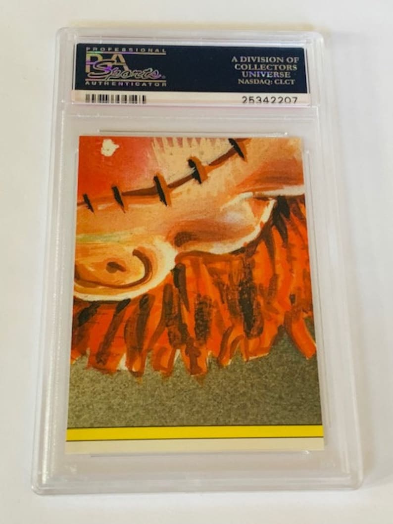 Puede incluir: Primer plano de una pintura abstracta colorida de una cara con heridas cosidas. La pintura est&aacute; en tonos de naranja, rojo y marr&oacute;n. El fondo es de color marr&oacute;n claro.