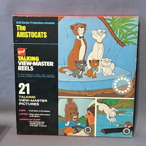 May include: A vintage "The Aristocats" View-Master reel set. The box features illustrations of the animated cats on a blue background. The box reads "TALKING VIEW-MASTER REELS" and "21 TALKING VIEW-MASTER PICTURES".