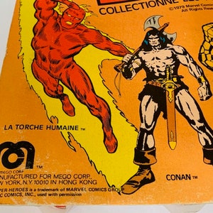 May include: A vintage action figure box featuring the Human Torch, Conan the Barbarian, and the Thing. The box is orange and yellow with black text. The text reads "La Torche Humaine TM", "Conan TM", and "Collection 1979 Marvel Comics Group All Rights Reserved".