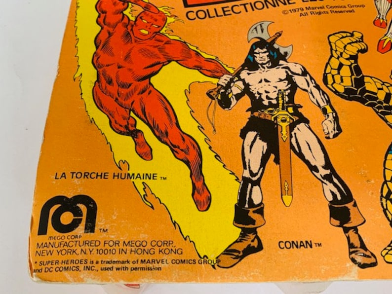 May include: A vintage action figure box featuring the Human Torch, Conan the Barbarian, and the Thing. The box is orange and yellow with black text. The text reads "La Torche Humaine TM", "Conan TM", and "Collection 1979 Marvel Comics Group All Rights Reserved".