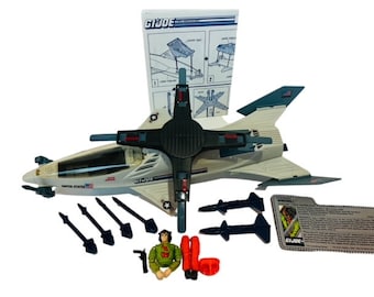 May include: A white and gray G.I. Joe  'Skystriker' toy jet with a black cockpit and a pilot figure. The jet has a United States flag on the side and comes with missiles and instructions.