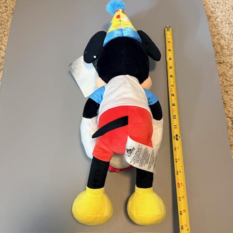 Pode incluir: Um brinquedo de pel&uacute;cia do Mickey Mouse usando um chap&eacute;u de festa. O brinquedo &eacute; preto, branco, vermelho, azul e amarelo. O brinquedo tem aproximadamente 46 cm de altura. O brinquedo tem uma etiqueta.