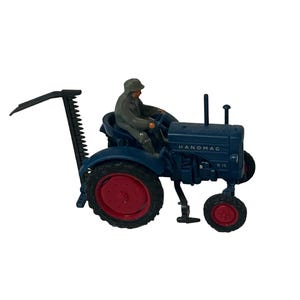 以下が含まれることがあります： 赤い車輪と黒いモアアタッチメントが付いた青いおもちゃのトラクター。トラクターには「HANOMAG R 16」という文字が側面に書かれています。