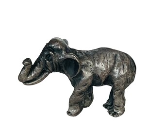 May include: A small, silver-colored elephant figurine. The elephant is standing with its trunk raised and its head tilted to the side. The figurine is detailed with textured fur and a realistic appearance.