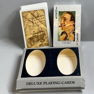 May include: A set of deluxe playing cards with a gray and black box. One deck features a sepia-toned cinema scene, while the other shows a joker with a cigar. The box reads "DELUXE PLAYING CARDS".