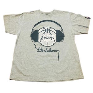 May include: A gray t-shirt with a black and white basketball graphic with headphones on it. The basketball has the Los Angeles Lakers logo on it. The text "L.A. Lakers" is written below the basketball.