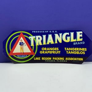 Puede incluir: Una etiqueta vintage azul y amarilla con un triángulo rojo que presenta a un niño de dibujos animados tocando un triángulo. La etiqueta dice "Triangle Brand" y enumera "Naranjas, Pomelos, Mandarinas, Tangelos". También dice "Producto de EE. UU." y "Lake Region Packing Association, Tavares, Florida".