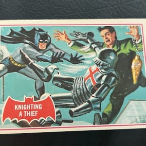 Könnte beinhalten: Eine Vintage-Comic-Sammelkarte mit Batman in einem blau-grauen Kostüm, der gegen einen Ritter in Rüstung kämpft. Die Karte trägt den Text "Knighting a Thief" auf einem roten Banner.