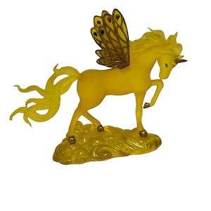 May include: A yellow unicorn figurine with gold wings and a cloud base. The wings have iridescent jewels.