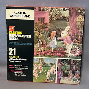 May include: A vintage "Alice in Wonderland" Talking View-Master Reels box. The box features a colourful illustration of Alice and the White Rabbit, with additional scenes below. The box reads "21 Talking View-Master Pictures" and includes the GAF logo.