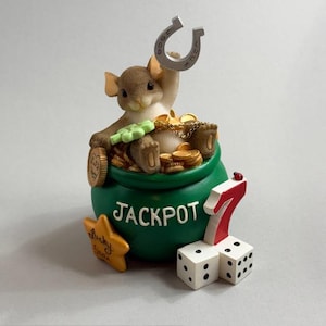 May include: A whimsical figurine featuring a brown mouse sitting in a green bag labeled "JACKPOT" filled with gold coins. The mouse holds a horseshoe and a four-leaf clover. A star and dice with the number 7 complete the lucky theme.
