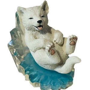 Op de afbeelding: Een wit ijsberenwelpje-beeldje met een speelse uitdrukking, zittend op een blauwe en transparante ijs sculptuur.