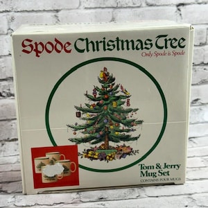 May include: A boxed set of four mugs, featuring the "Spode Christmas Tree" design. The box has a green and white color scheme with the text "Spode Christmas Tree" and "Tom & Jerry Mug Set". The mugs are decorated with a Christmas tree design.