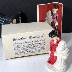 Könnte beinhalten: Eine weiße Box mit blauem Text, der "Sebastian Miniatures" und "America's foremost Miniatures" lautet. Die Box ist geöffnet und zeigt eine Miniaturfigur einer Frau in einem roten Kleid, die eine weiße Büste hält. Die Figur steht auf einem weißen Sockel.