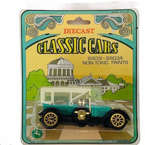 Könnte beinhalten: Ein türkisfarbenes Spielzeugauto aus Metall mit weißem Dach und goldenen Rädern. Das Auto befindet sich auf einer gelben und grünen Karte mit den Worten "Classic Cars" und "S8031-S8034 Ungiftige Farben" darauf gedruckt. Die Karte zeigt auch ein Gebäude mit einer Kuppel.