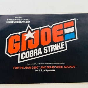 Puede incluir: Una caja de cartucho de juego negra y roja para Atari 2600 y Sears Video Arcade. La caja presenta el logotipo de G.I. Joe con las palabras "Cobra Strike" debajo. El texto "Para 1, 2 o 3 jugadores" está en la parte inferior de la caja.