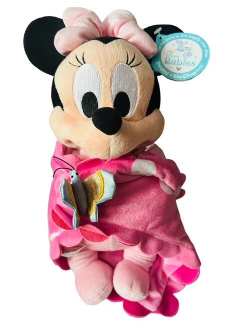 May include: Pink and black plush Minnie Mouse doll wearing a pink blanket with a butterfly design. The doll has a pink bow and is holding a butterfly. The tag reads "Disney Babies".