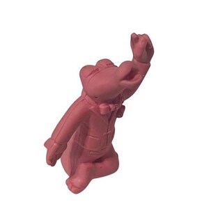 May include: A pink rubber figurine of a cartoon character wearing a tuxedo. The character is standing on one leg with its other leg bent and its arm raised in the air.