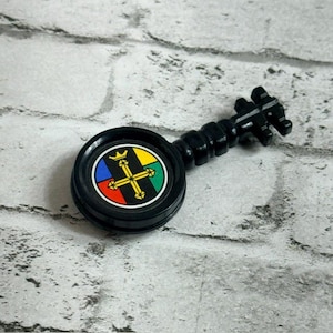 Pode incluir: Um porta-crachá preto em forma de chave com um centro circular apresentando um emblema de coroa e cruz amarela. O emblema está sobre um fundo dividido em quatro quadrantes nas cores azul, amarelo, verde e vermelho. A chave tem um cabo.