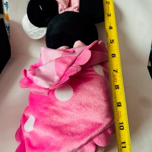 May include: Pink and black plush toy of a mouse wearing a pink bow and a pink blanket with white polka dots. The toy is approximately 12 inches tall.
