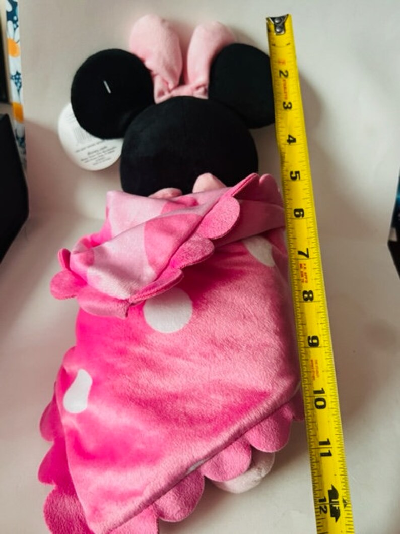 May include: Pink and black plush toy of a mouse wearing a pink bow and a pink blanket with white polka dots. The toy is approximately 12 inches tall.