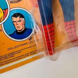 May include: A vintage action figure of Spider-Man in a red and blue suit with a web design. The figure is packaged in a plastic blister pack with a yellow cardboard backing. The backing features images of Thor and Mr. Fantastic, along with the Mego Corp logo and text that reads "Collectionne les tous" and "Conformite aux normes de securite garantie par Lutece Trading International. Fabrique a Hong Kong. All Marvel Characters are trademarks of the Marvel Comics Group, Inc. 1979. All rights reserved. of Cadence Industries Corporation."