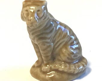 May include: A small ceramic figurine of a tiger sitting down. The tiger is brown and white with stripes. The figurine is about 3 inches tall.