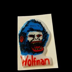 May include: A blue and red sticker with a cartoon image of a werewolf with the text "Wolfman" underneath.
