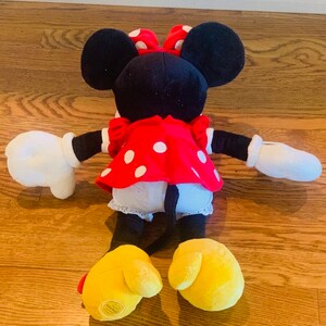 May include: A plush toy of Minnie Mouse wearing a red dress with white polka dots and a red bow. The toy has black ears, yellow shoes, and white gloves.