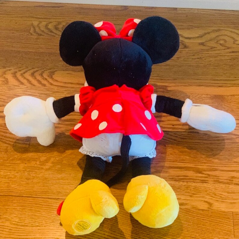 May include: A plush toy of Minnie Mouse wearing a red dress with white polka dots and a red bow. The toy has black ears, yellow shoes, and white gloves.