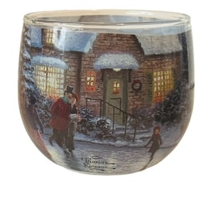 May include: A glass candle holder with a winter scene featuring a snow-covered house with lit windows, a couple walking in the snow, and a child walking in the distance. The candle holder has a Thomas Kinkade signature at the bottom.