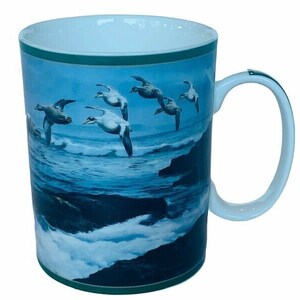 May include: White ceramic mug with a green rim and a blue and green image of seabirds flying over a blue ocean with white waves crashing on a rocky shore.