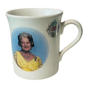 Puede incluir: Taza de cerámica blanca con una imagen de la reina Isabel II con una corona y un vestido amarillo. La taza tiene una pegatina que dice "Prince William Patron, C.O. The Prince's Trust" con una bandera del Reino Unido.