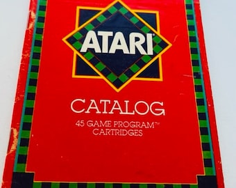 May include: A red Atari Video Computer System catalog with a green and black checkered border. The Atari logo is a diamond shape with the word "ATARI" in white letters. The text "CATALOG" is in white letters and the text "45 GAME PROGRAM™ CARTRIDGES" is in white letters.